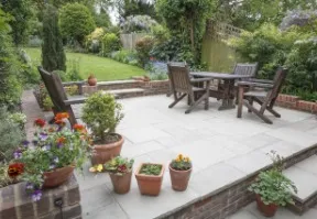 Patio with wooden furniture, flowerpots, and a lush garden in the background.