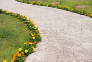 Stone walkway curves through a grassy area, lined with yellow and orange flowers.