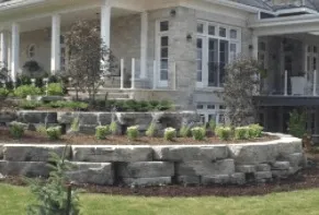 Stone retaining wall with plants in front of a house with a porch.