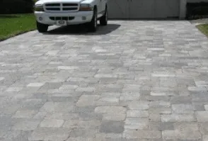 White SUV parked on a paved driveway with gray and beige interlocking bricks. Garage is in the background.