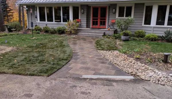 Pathway leading to a gray house with a red door, flanked by landscaping and small rocks.