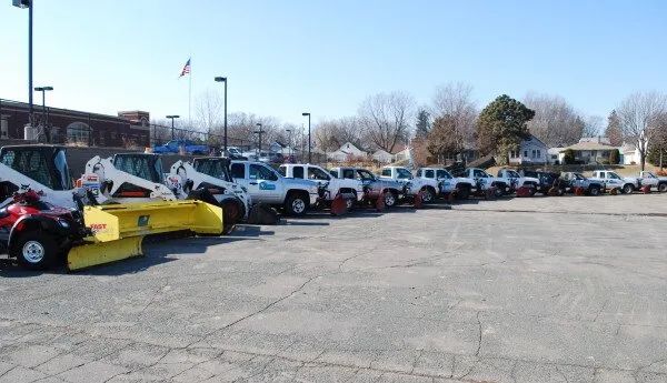 A line of white pickup trucks and utility vehicles parked on asphalt, some with plows.