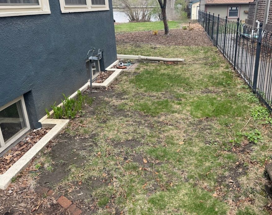 A dark blue home exterior with a concrete landscape border along the foundation, transitioning into a patchy, sparse lawn.