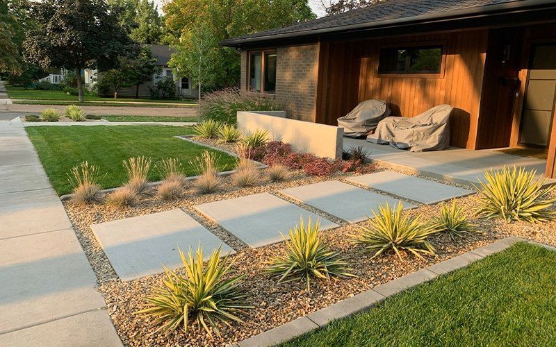 A modern home's landscaping features square stepping stones, gravel beds, and green grass.