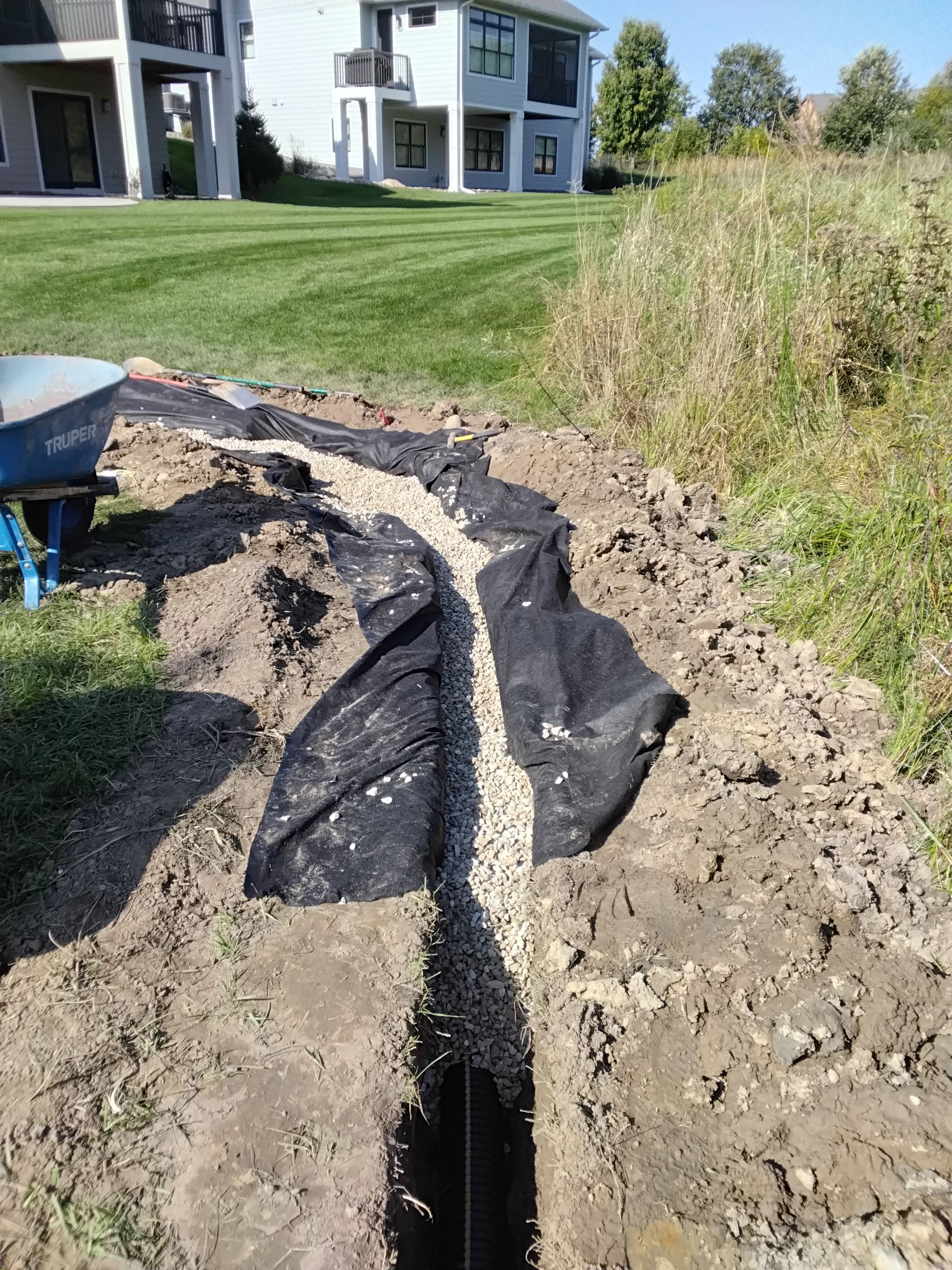 Crew backfilling French drain pipe with rock