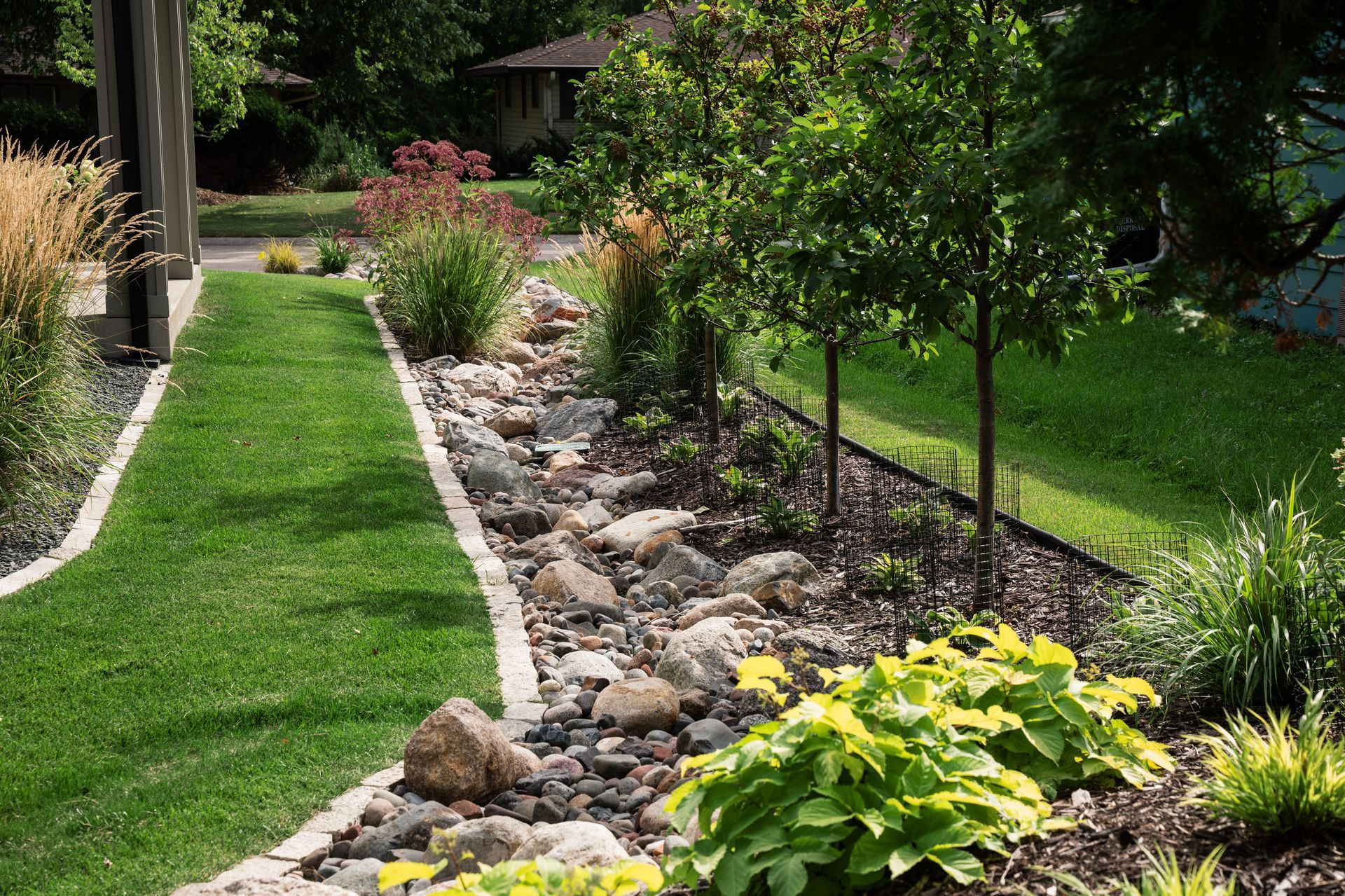 very nice looking river rock and boulder dry creek bed landscaping with trees, grasses and plants in MN designed by KG Landscape