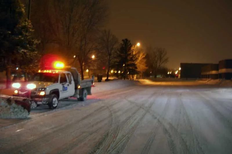 A snow plow is driving down a snow covered road.