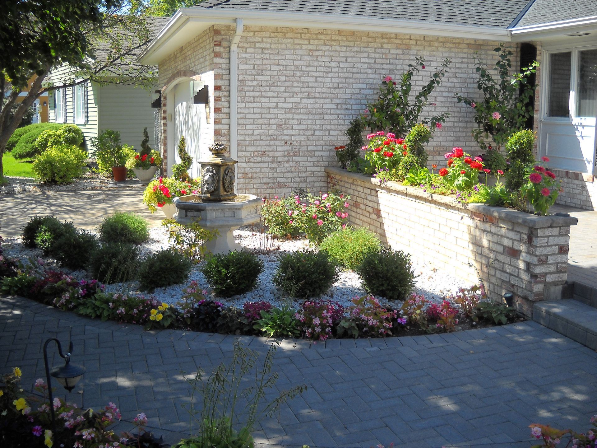 Brick house with landscaped flower beds, water fountain, and paved walkway.