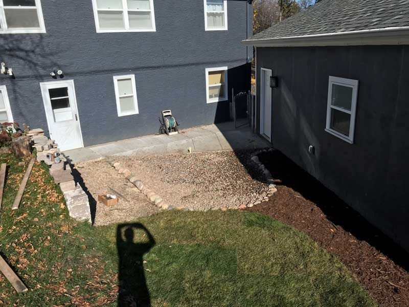 Backyard with a dark blue house, patio area with gravel, and shed.