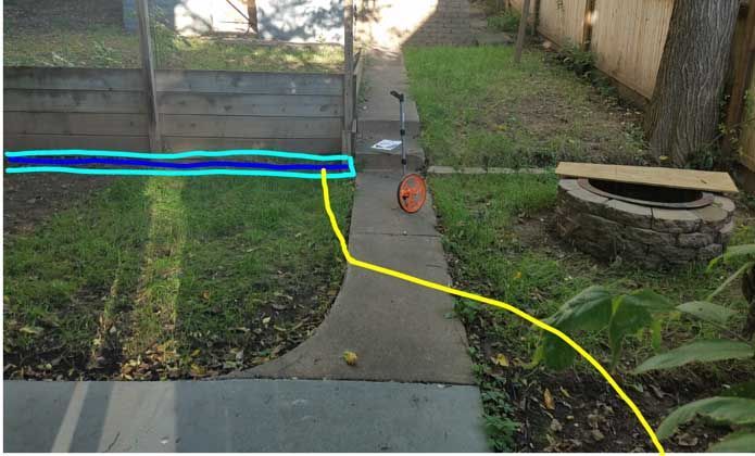 Concrete path through grassy yard, wooden fence, fire pit. Yellow line on path, blue line on fence.