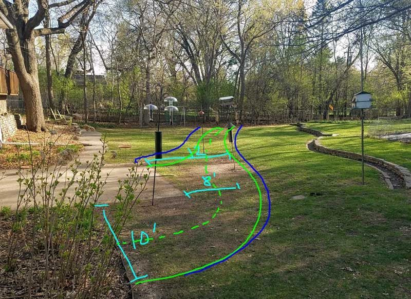 A backyard lawn with a curved path outlined in green, a driveway on the left, and bird feeders.