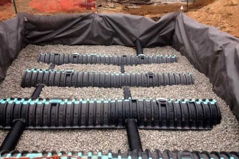 A row of black pipes are lined up in a pile of gravel.