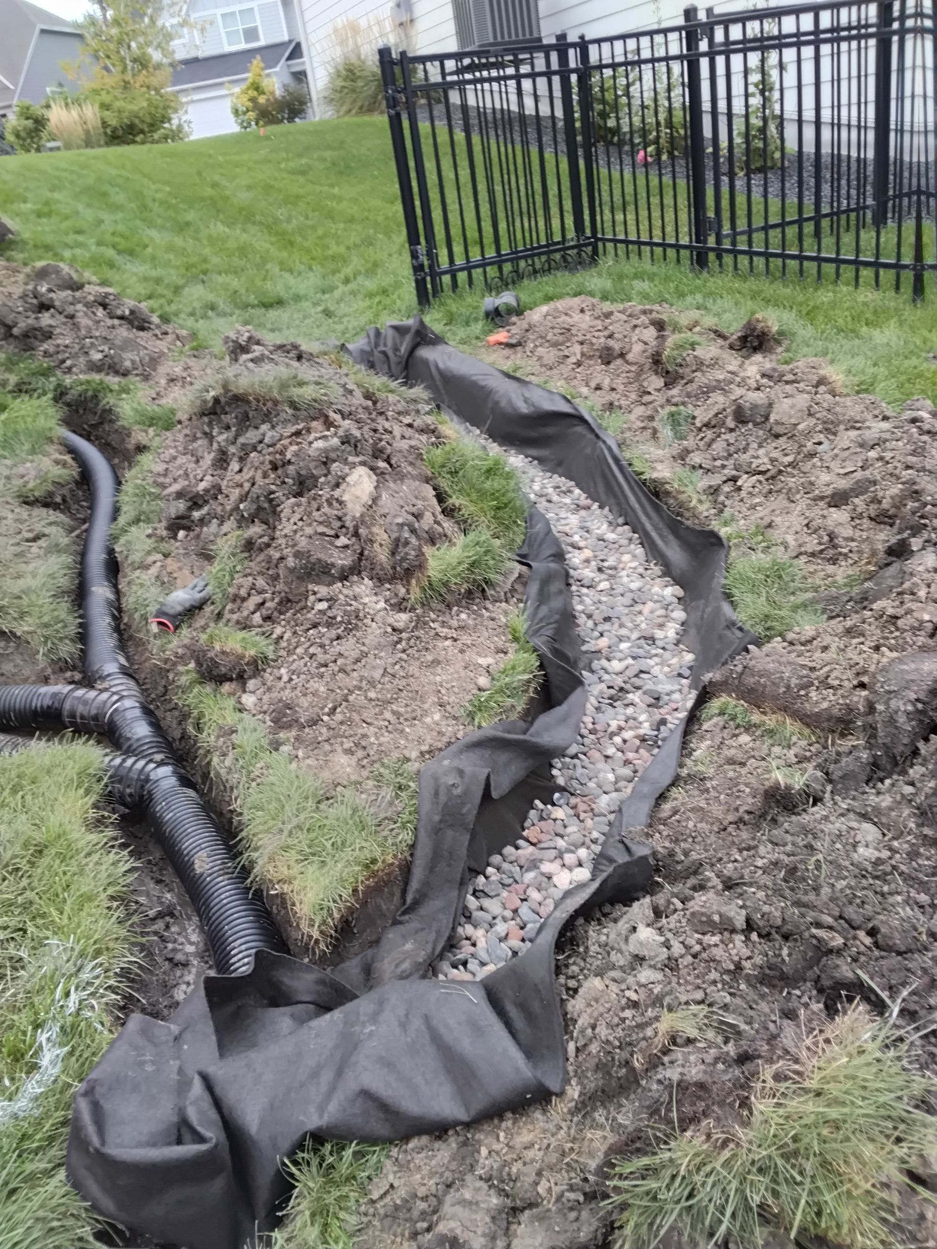 Underground downspout drainage system connected to a French drain in a wet side yard area near the backyard gate.