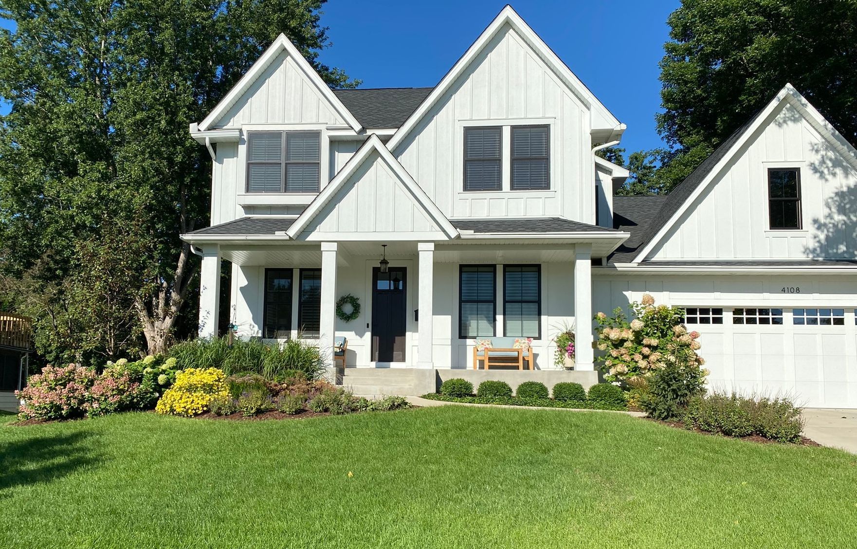 White farmhouse with black shutters and a black door, green lawn and landscaping.