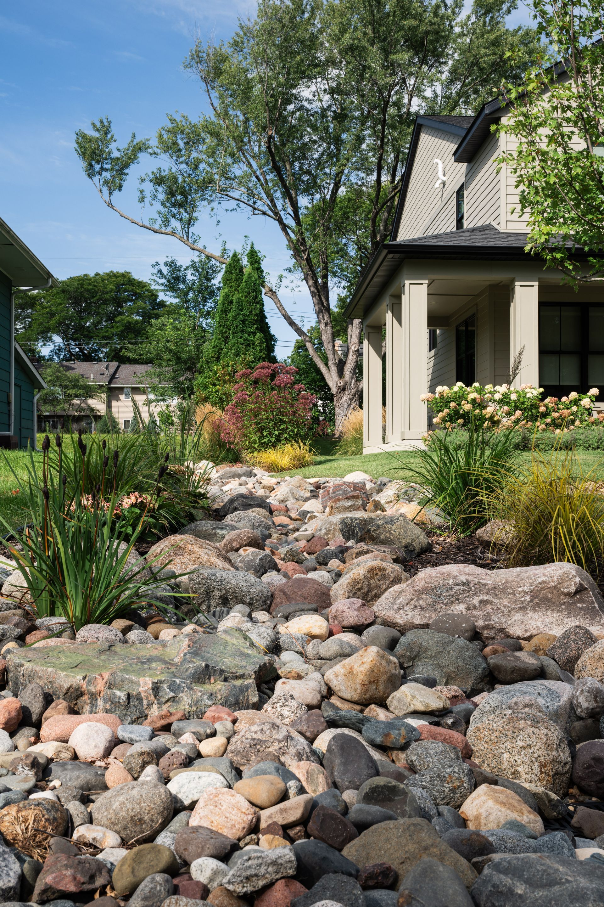 Lush green lawn with a rock garden border leading to a stone patio with a tree in front.