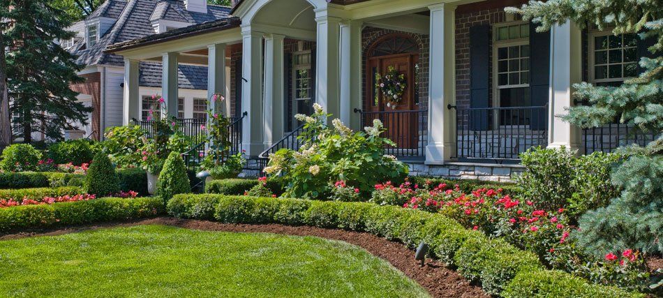 Well-manicured front yard with a landscaped garden in front of a house with a porch and columns.