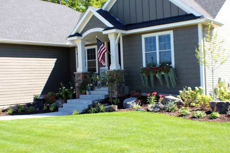 Front yard boulder outcropping with flowers, a redbud tree, and an American flag in Chanhassen MN