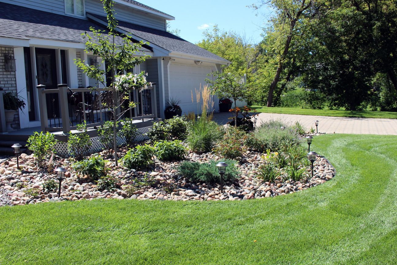 Low-maintenance river rock bed with curved edging softening a front deck, Tina crab tree and catmint, Minneapolis