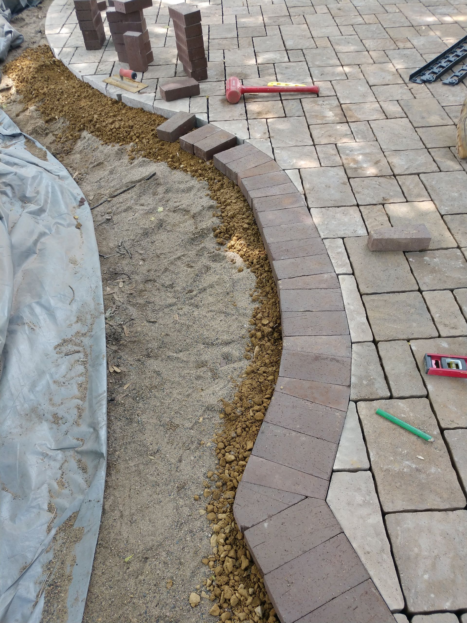 Pathway edging with bricks being installed, next to a stone paver patio.