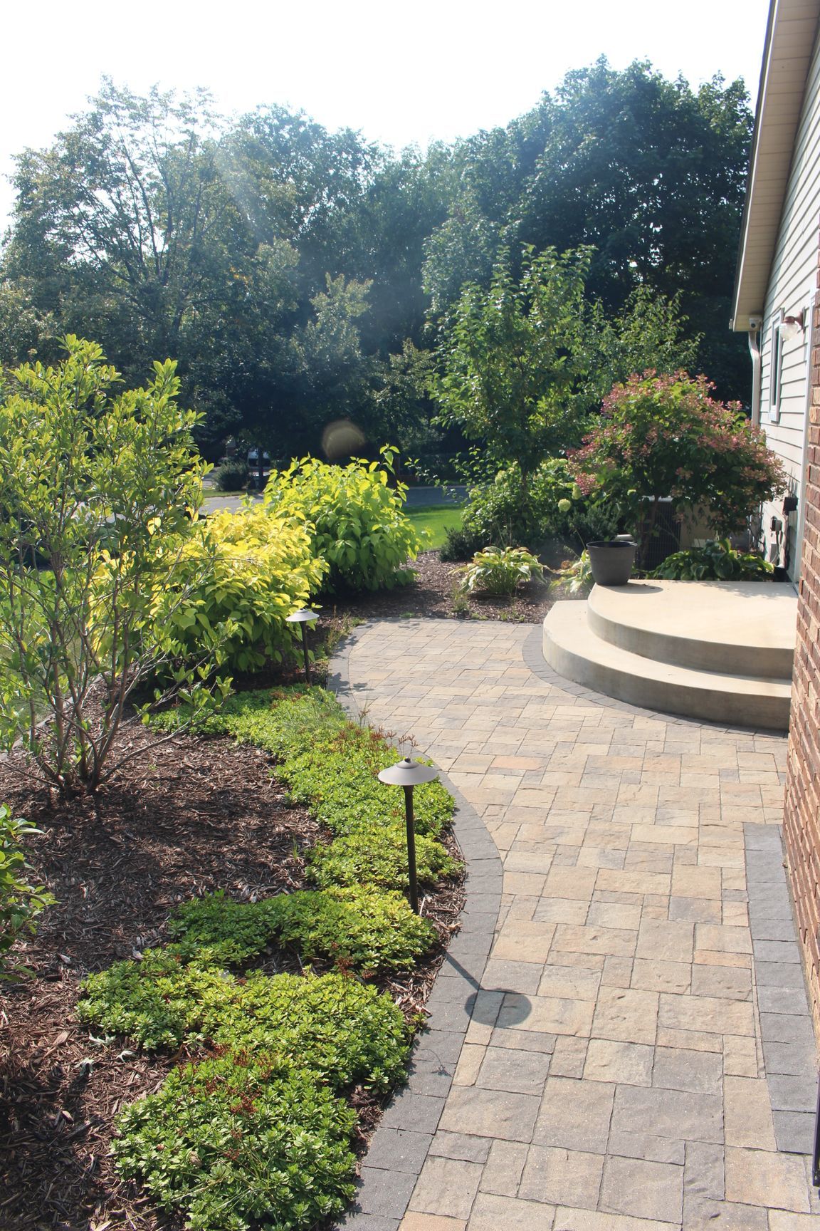 Quarter-circle concrete landing and steps off a sliding door to a paver walkway with plantings and path light, Shoreview MN