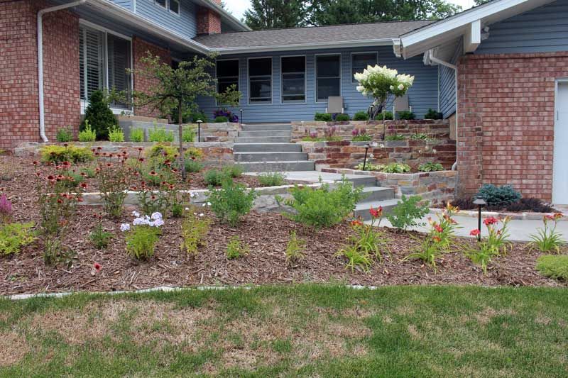 Exterior view of a house with tiered landscaping and stairs leading to the front door, with various plants in bloom.