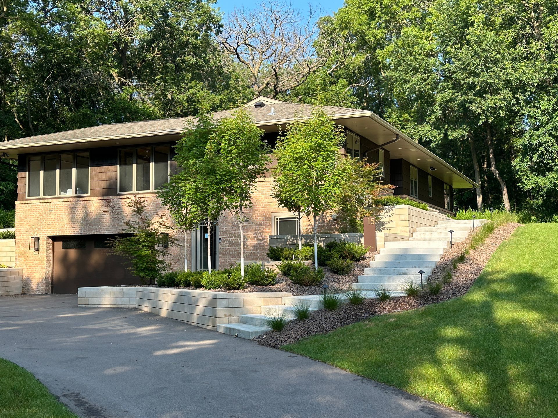 A tan brick home with a flat roof, dark garage door, and a light stone staircase leading to the front entry.