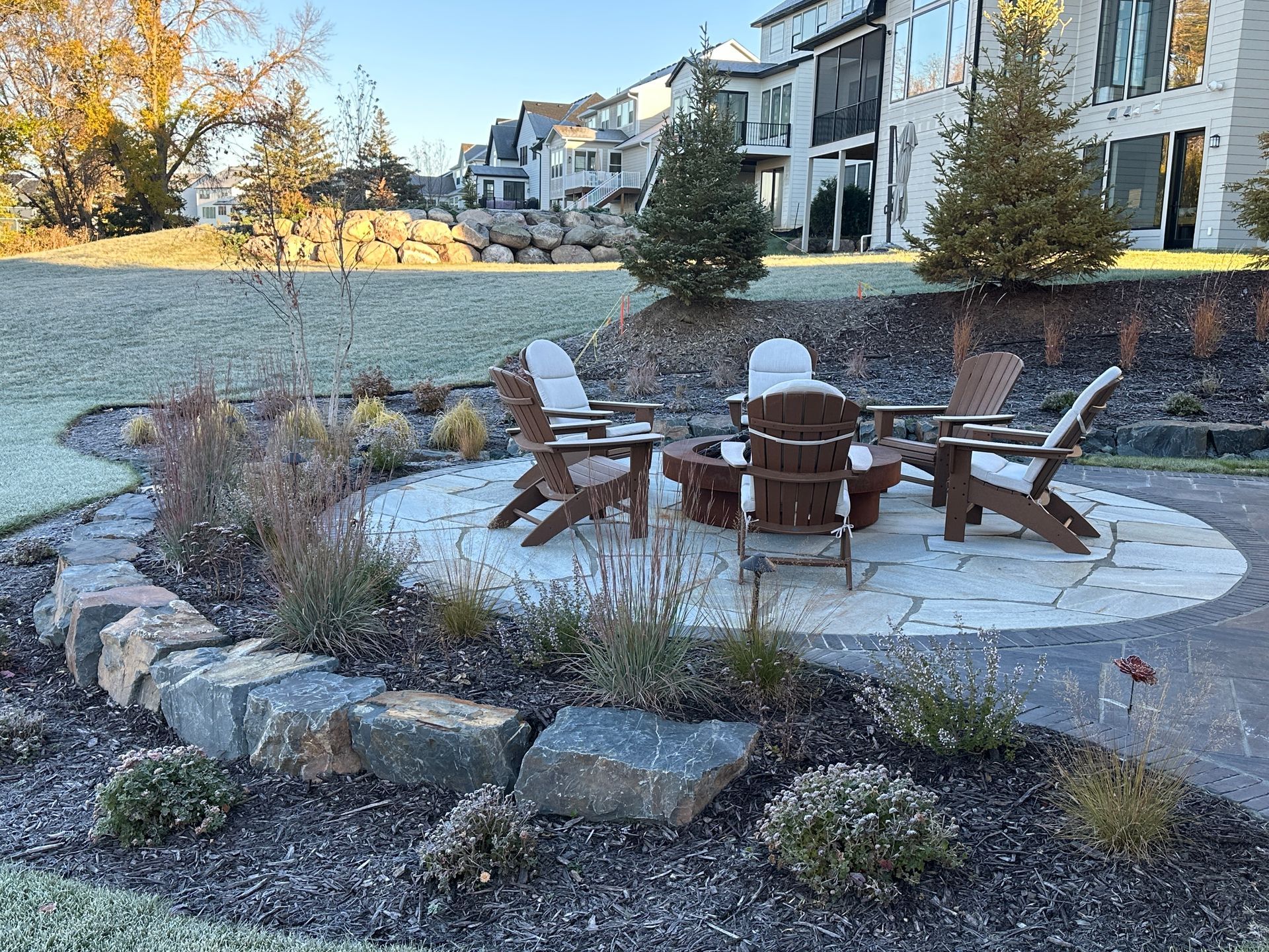 Circular stone patio with a fire pit, built into a sloped backyard with boulder walls
