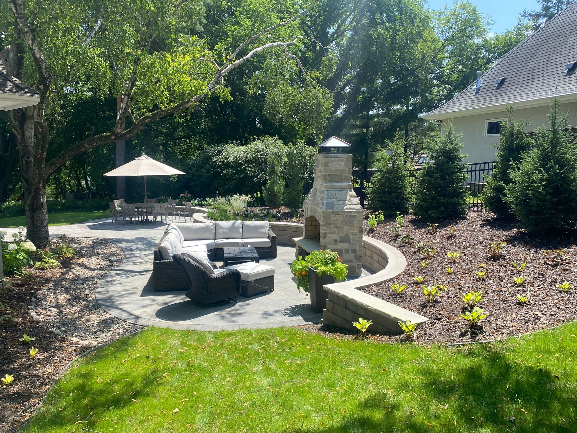 Outdoor patio with seating, fireplace, and dining area surrounded by greenery.