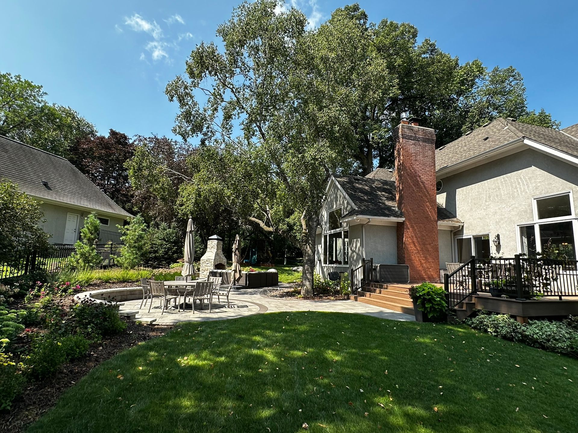 New backyard deck landing and patio with outdoor living space table and fireplace and wall and birch tree in Minnetonka MN designed by KG Landscape 