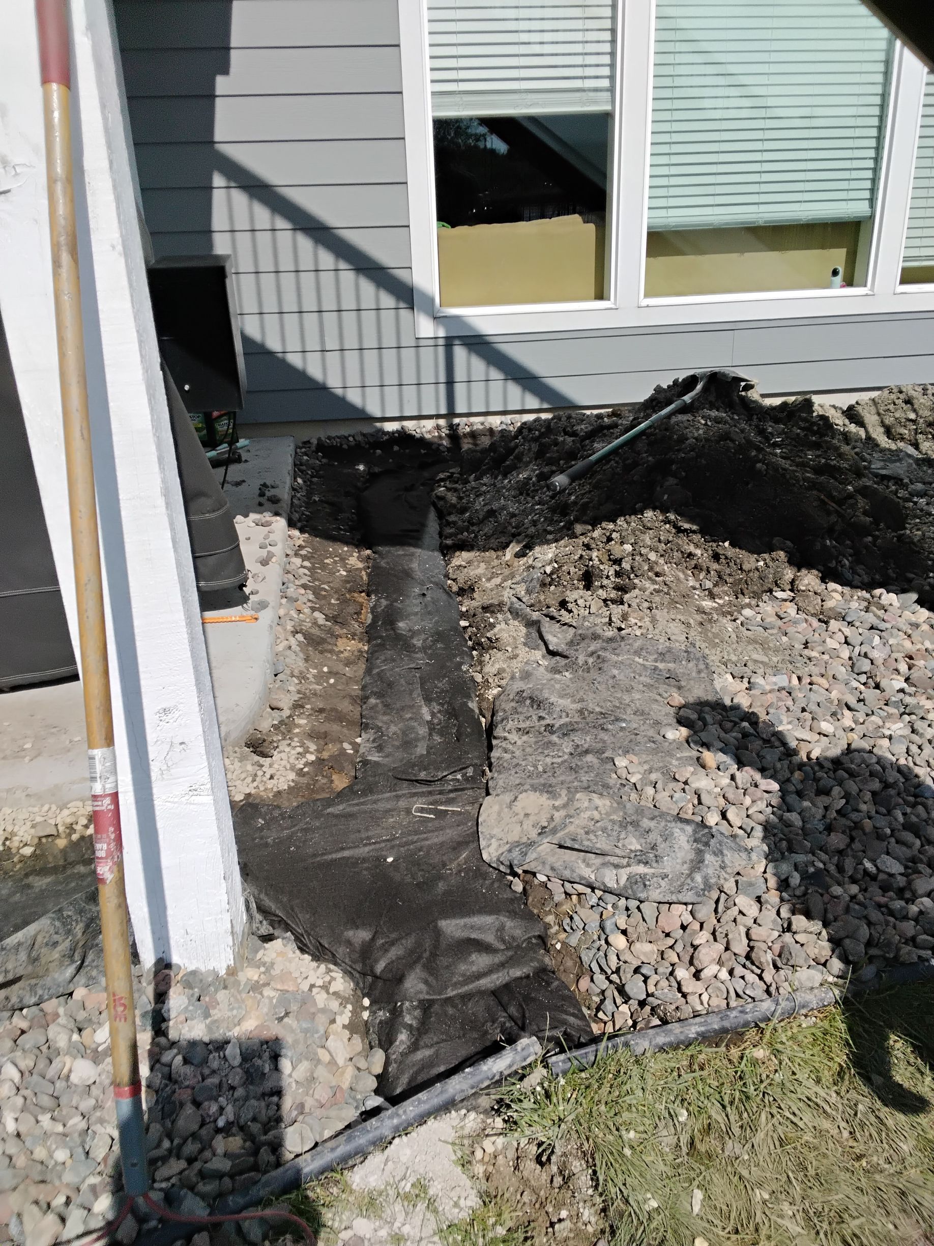 During - our crew wrapping fabric around a French drain being installed around a backyard patio in Plymouth MN 