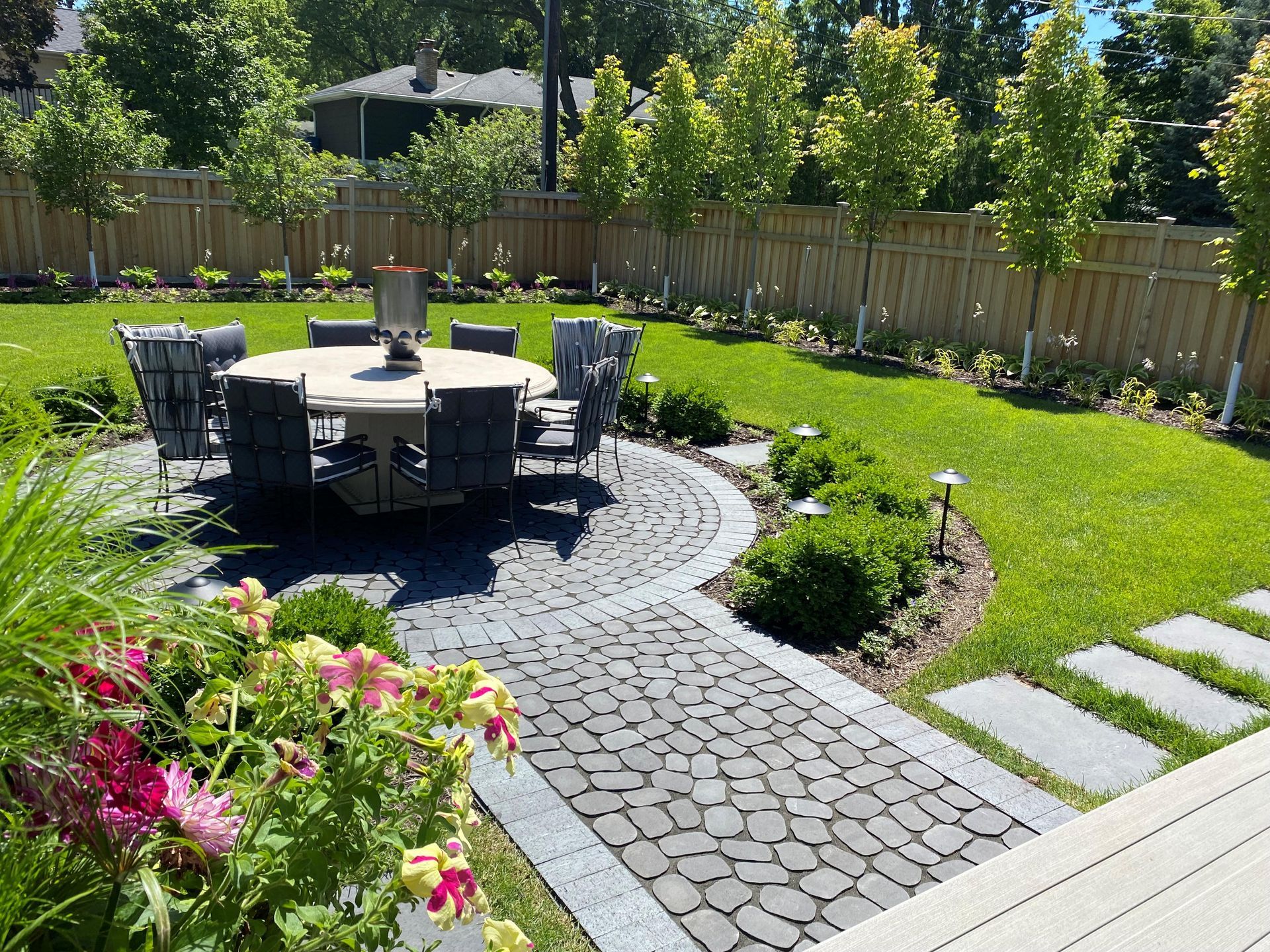 Backyard patio with cobblestone pathway, dining table, lush green grass, and trees.