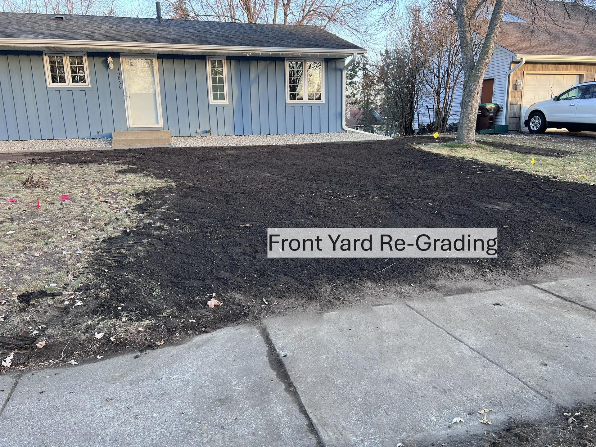A blue house with a freshly regraded, dark soil front yard leading to a concrete sidewalk.
