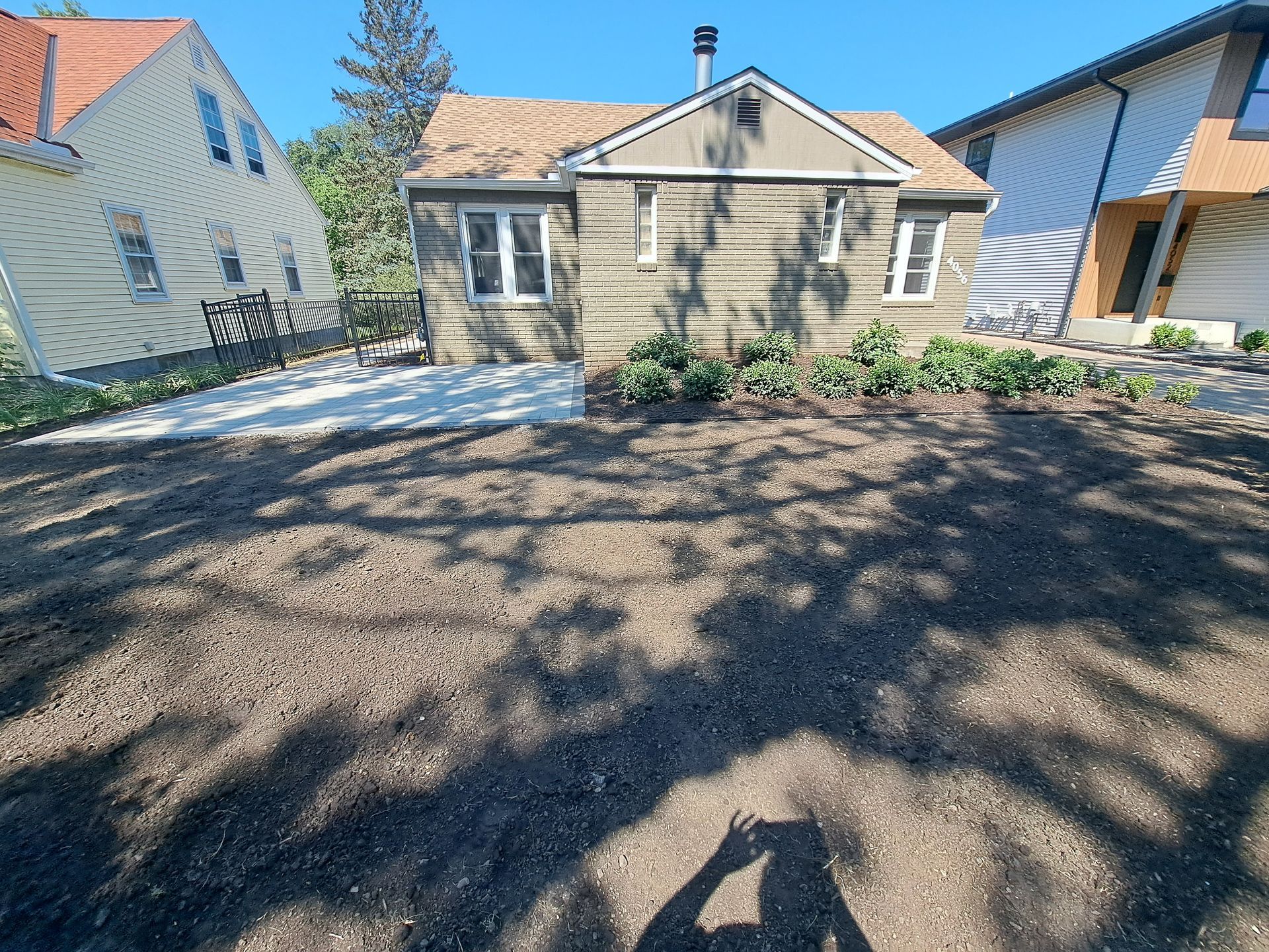 A freshly leveled dirt yard with a new concrete patio slab beside a house under a clear blue sky.