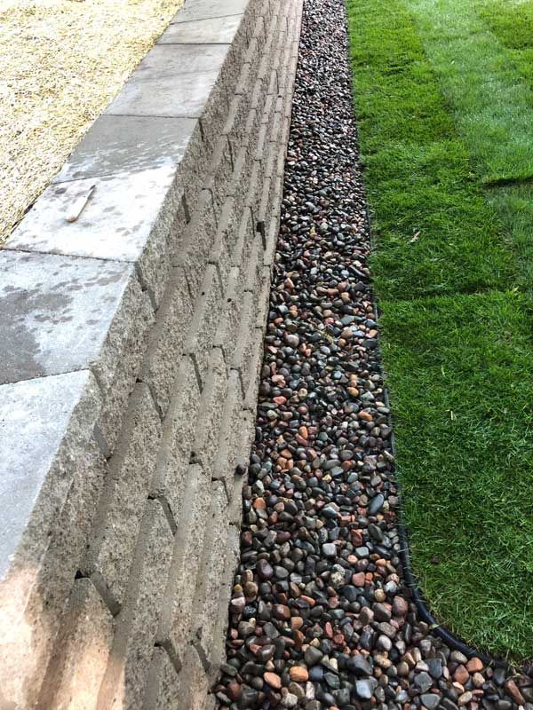 Stone retaining wall with a gravel bed, bordered by green grass.