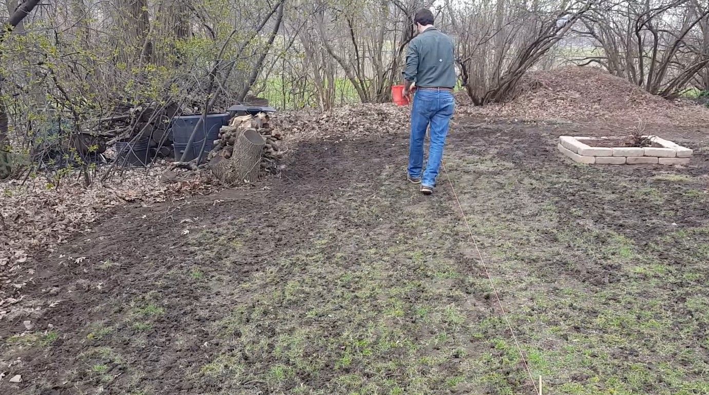 A man is walking through a muddy field with a bucket in his hand.