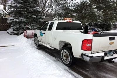 White snowplow truck clearing a snow-covered residential driveway.