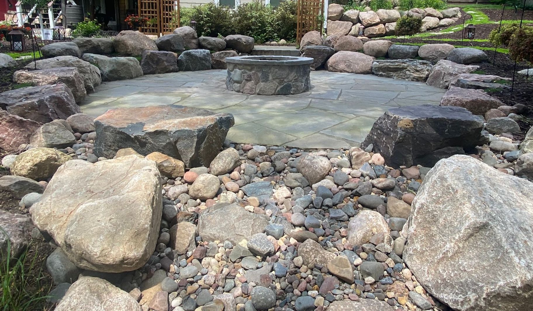 Stone fire pit surrounded by large rocks and gravel in a landscaped backyard.