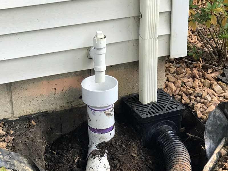 White PVC pipe installation near house with gutter and drain.