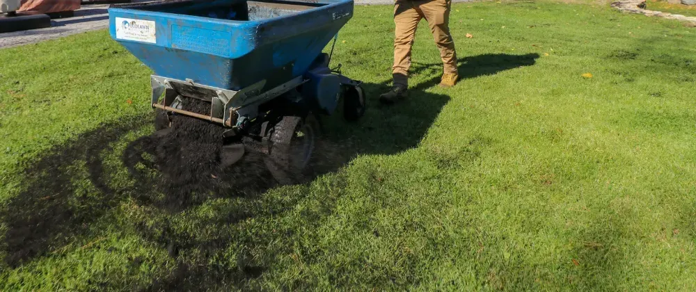Top dresser spreading thin layer of rich topsoil over lawn