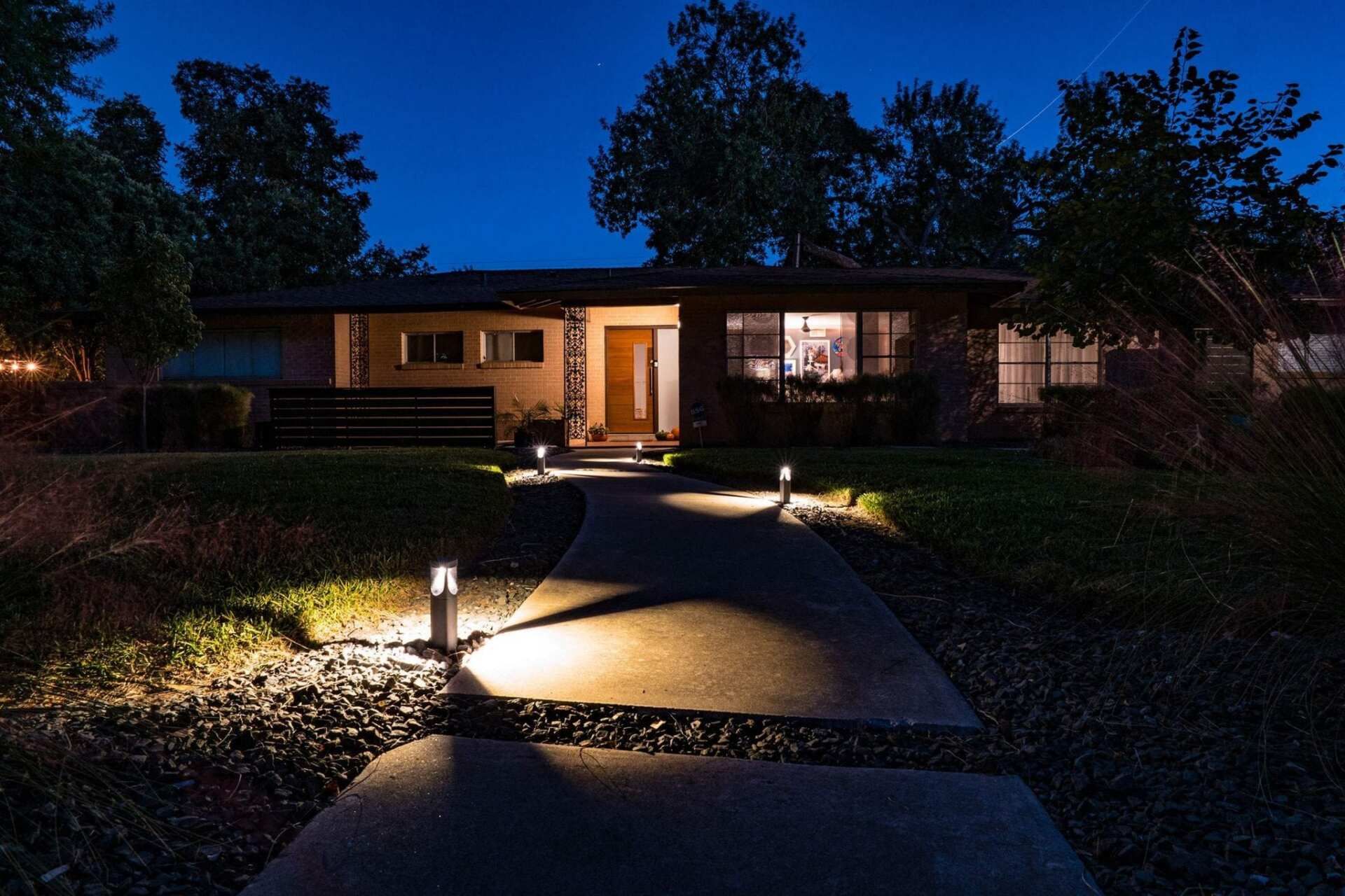 Night view of a house with a lit pathway leading to the front door, surrounded by trees.