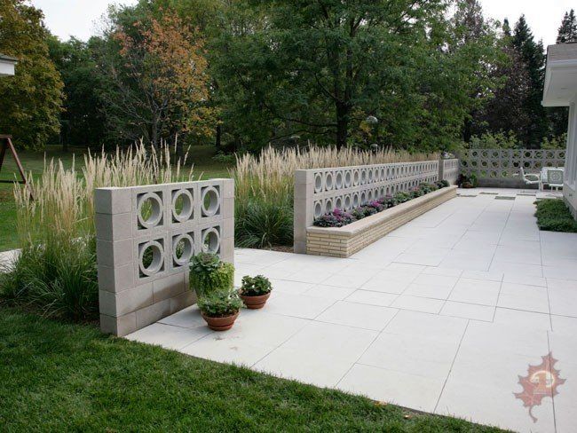Concrete block wall with circle cutouts and a small garden, on a patio next to grass and tall grass plants.