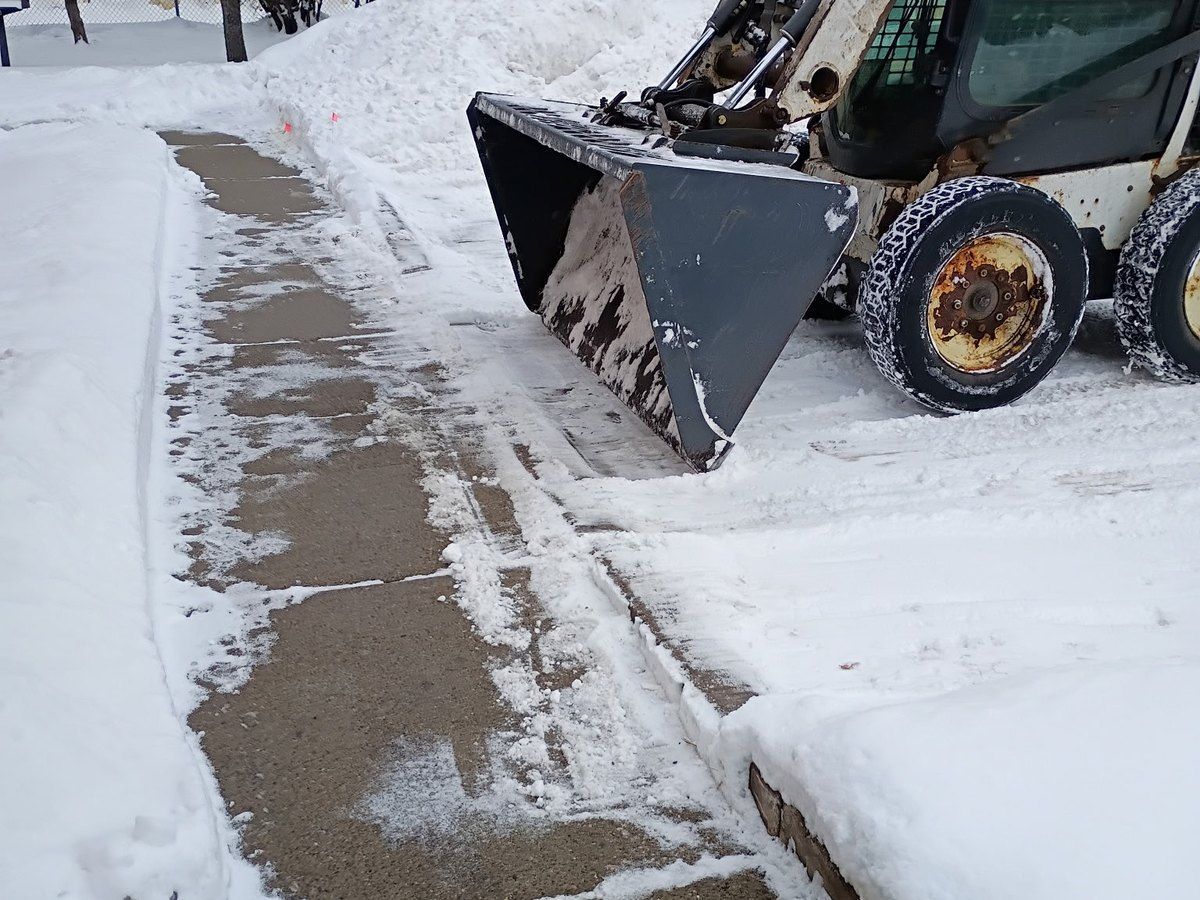 Concrete walk cleared to bare pavement with plowed snow banked along one side