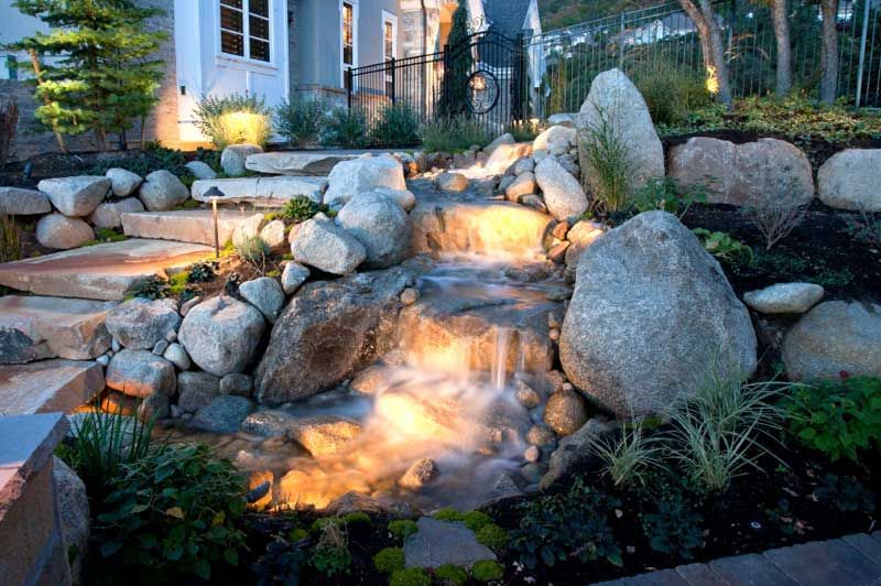 A waterfall is surrounded by rocks and is lit up at night.