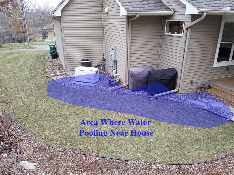 Water pooling near a house, blue shaded area. Gravel path with cooler, grass, and house siding.