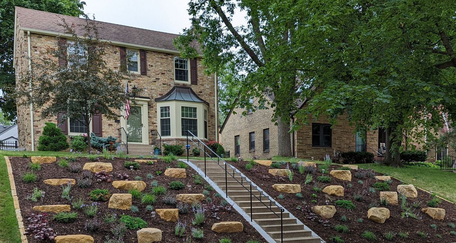 A large brick house with landscaped slope hillside front yard hill with plantings and boulder outcroppings in Minneapolis MN