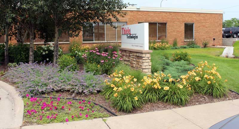 Sign in front of a brick building, surrounded by landscaping and flowers.