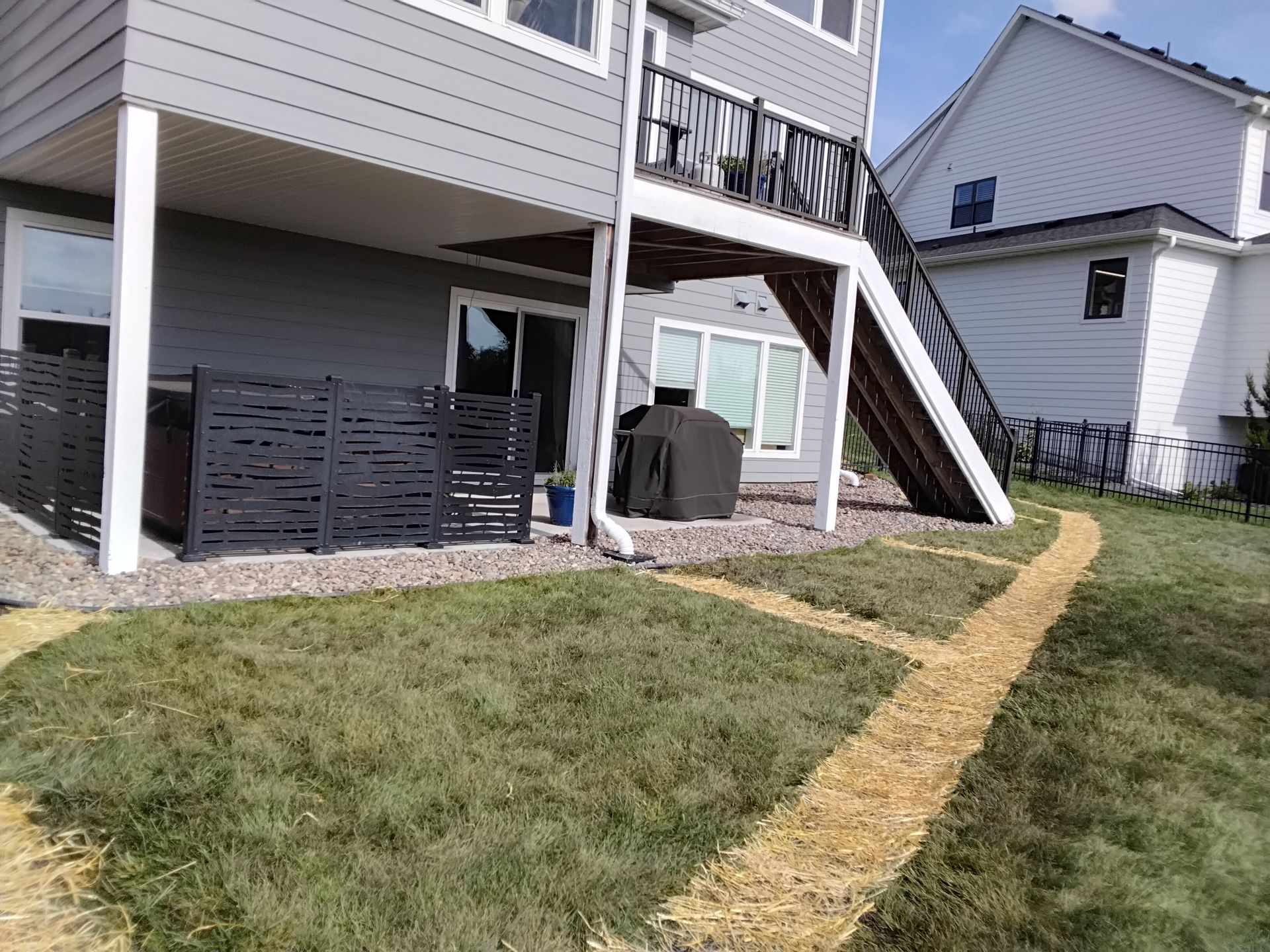 Completed underground downspout drain installation with restored lawn, fresh seed and straw matting, repaired rock edging, and clean finished landscape.