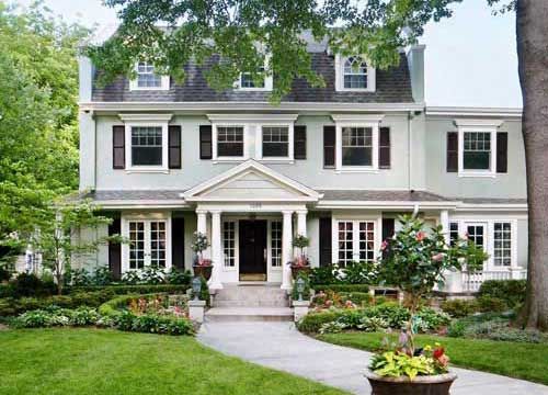 A large house with a lush green lawn pretty flowers and shrubs in front of it.