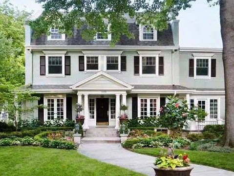Two-story house with green exterior, black shutters, and a landscaped front yard with a curved walkway.
