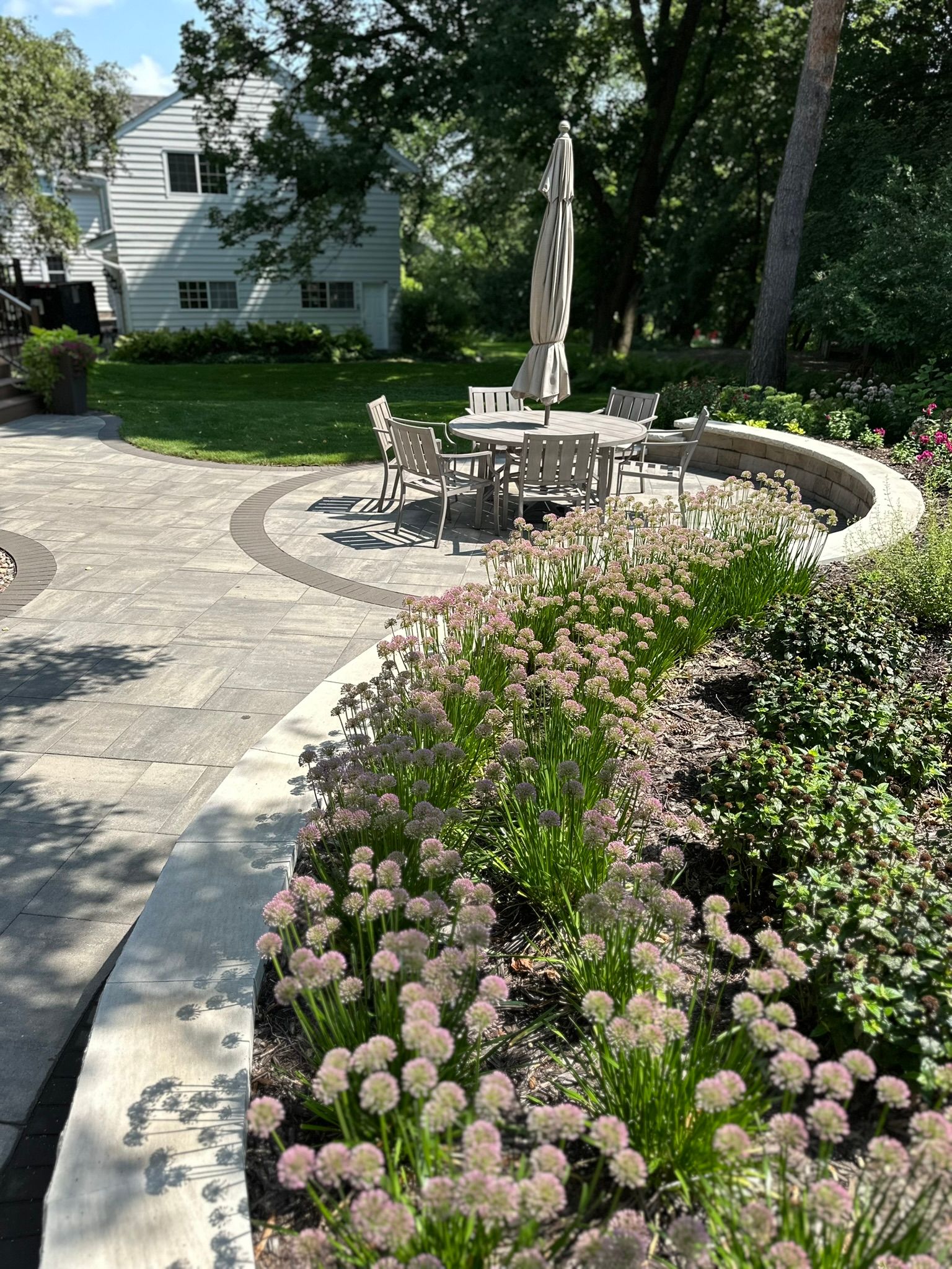 Round dining space on patio with tables surounded by landscaping. 